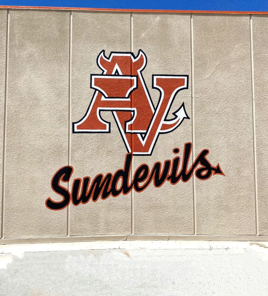 A painted school mural of the orange and black Sundevils mascot logo on a beige textured concrete exterior wall.