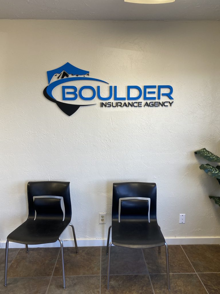 Dimensional blue and black Boulder Insurance Agency logo mounted on an interior office wall with two chairs nearby.