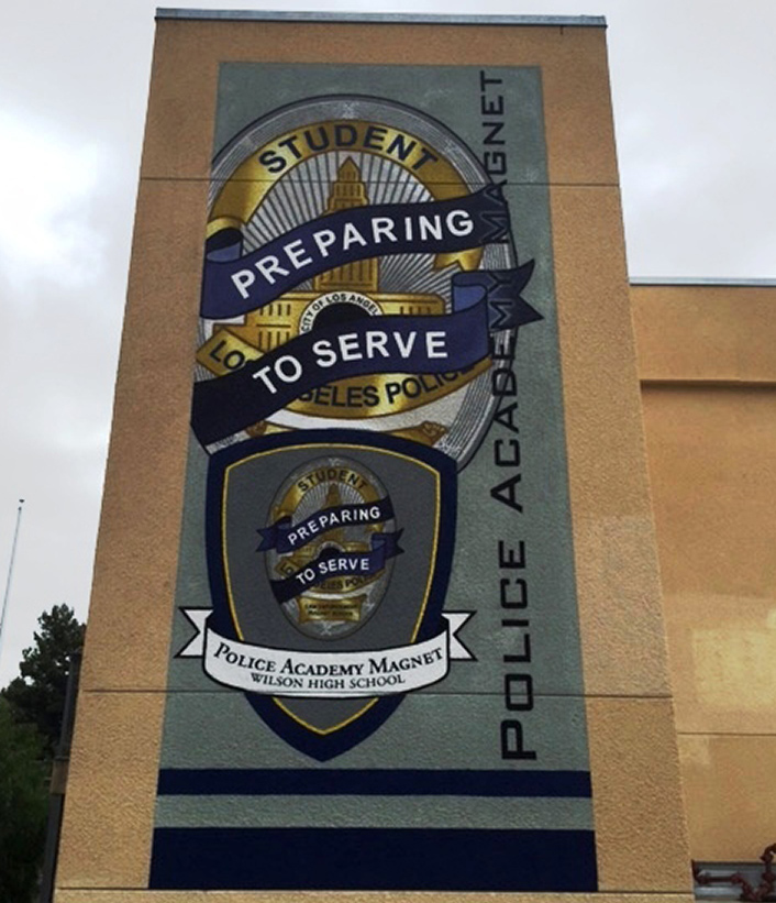 A large hand-painted mural on a school building wall featuring the Los Angeles Police Academy Magnet insignia.