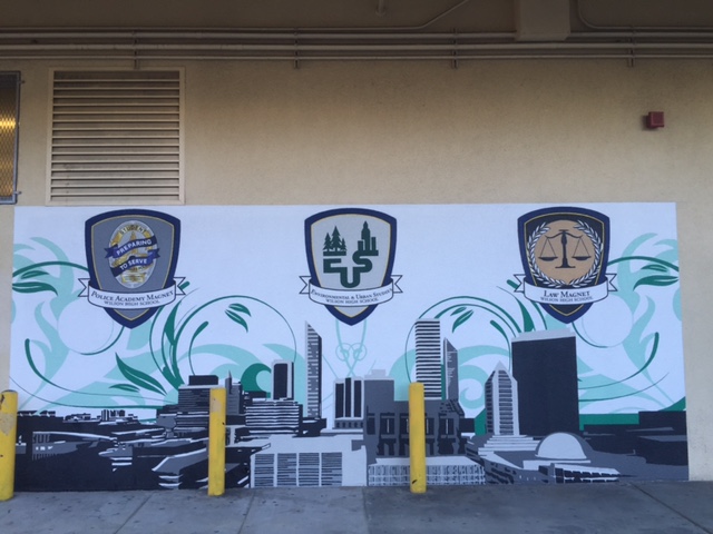 Mural on a wall featuring three school academy crests above a graphic silhouette of a city skyline.